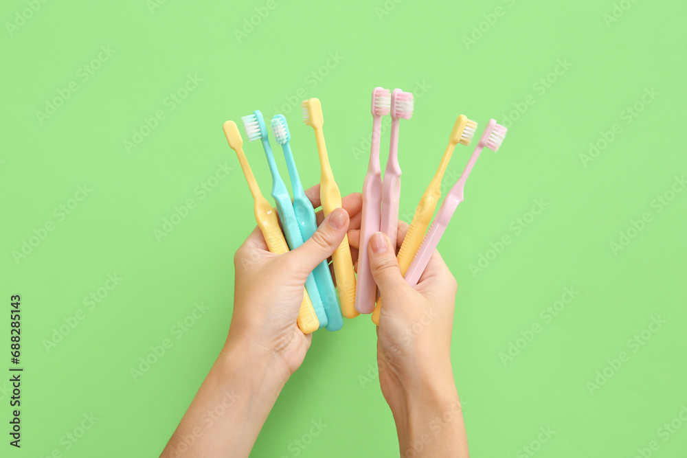 Female hands with colorful plastic toothbrushes on green background. Female hands with colorful plastic toothbrushes on green background.