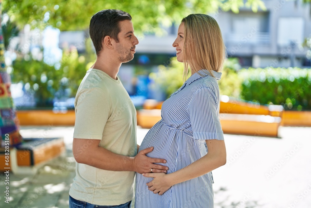 Man and woman couple standing together touching belly at park Man and woman couple standing together touching belly at park