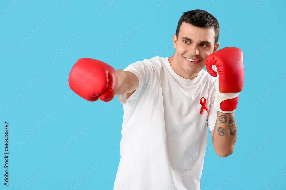 Young man with red ribbon and boxing gloves on blue background. World AIDS day concept Young man with red ribbon and boxing gloves on blue background. World AIDS day concept