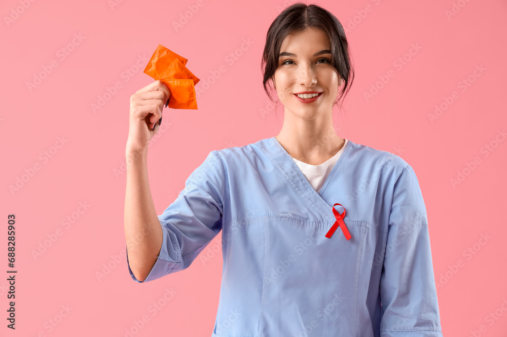 Young female doctor with red ribbon and condoms on pink background. World AIDS day concept Young female doctor with red ribbon and condoms on pink background. World AIDS day concept