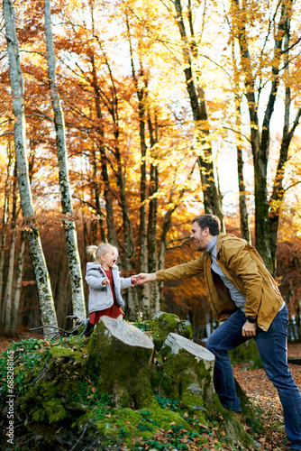 Dad extends his hand to a little laughing girl standing on stumps in the forest