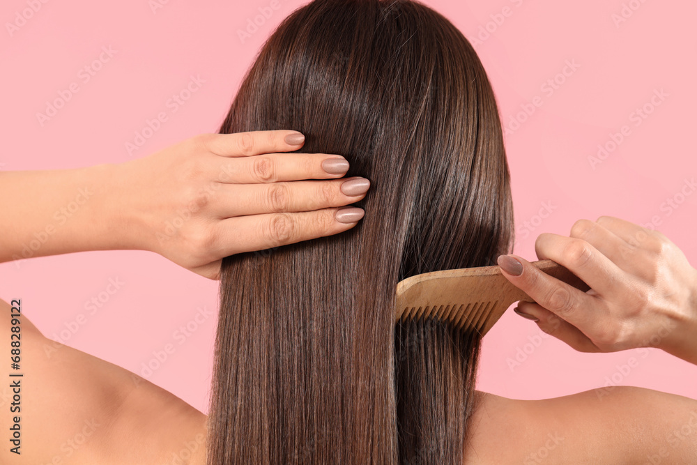 Fototapeta premium Young brunette woman combing beautiful hair on pink background, back view