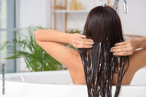 Young brunette woman applying hair product in bathroom, back view photo