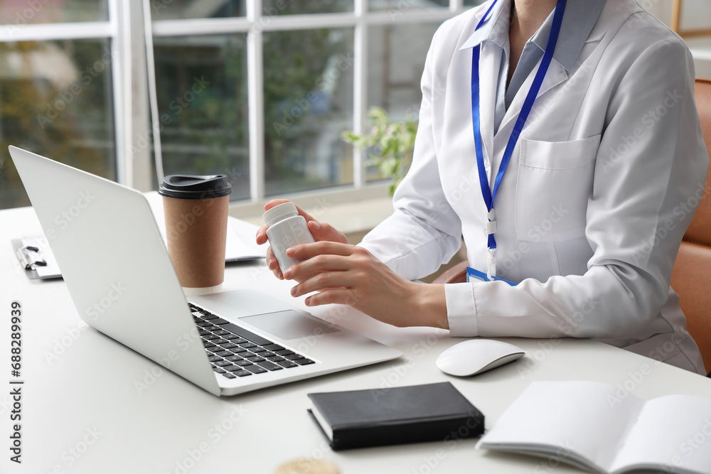 Female doctor with pill bottle working at table in clinic, closeup Female doctor with pill bottle working at table in clinic, closeup