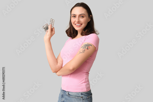 Beautiful young woman with condom and birth control pills on grey background.  Safe sex concept