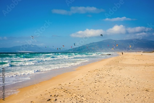 Soaring kite surfers and beach with Atlantic ocean and golden sand on background of mountains.