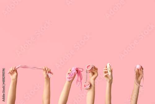 Female hands with different sex toys on pink background
