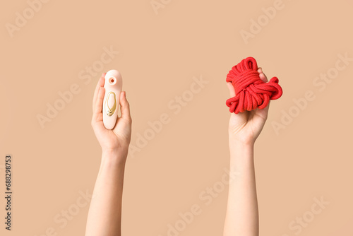 Female hands with vibrator and rope from sex shop on color background, closeup