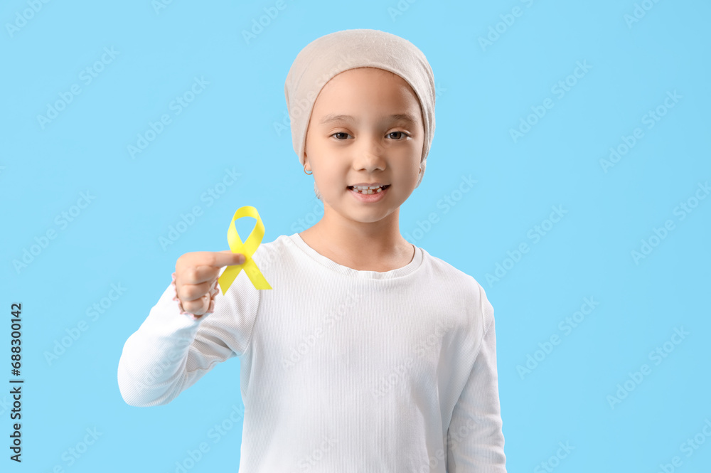 Little Asian girl after chemotherapy with ribbon on blue background. Childhood cancer awareness concept Little Asian girl after chemotherapy with ribbon on blue background. Childhood cancer awareness concept