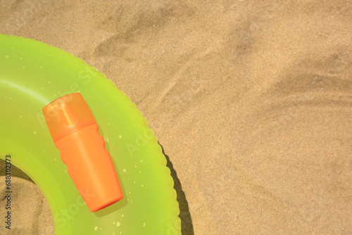 Sunscreen and inflatable ring on sand, top view with space for text. Sun protection care