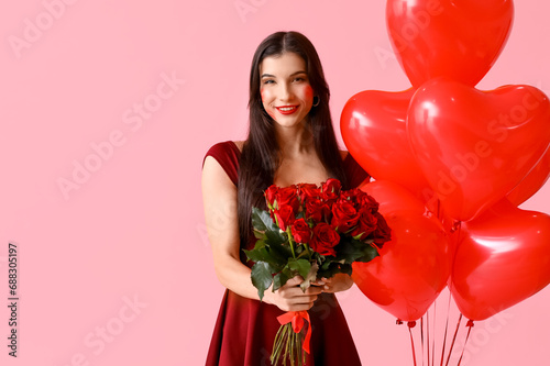 Happy young woman with kiss marks on her face holding bouquet of roses and heart shaped air balloons on pink background