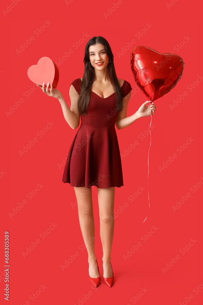 Beautiful young woman with kiss marks on her face holding gift box and heart shaped air balloon on red background Beautiful young woman with kiss marks on her face holding gift box and heart shaped air balloon on red background