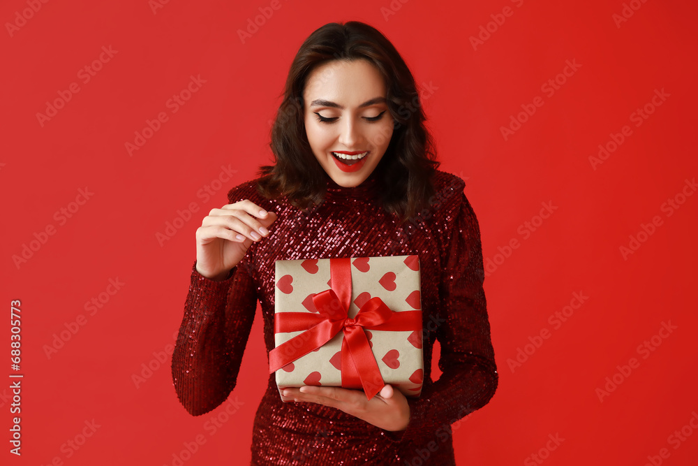 Surprised young woman with gift box on red background Surprised young woman with gift box on red background