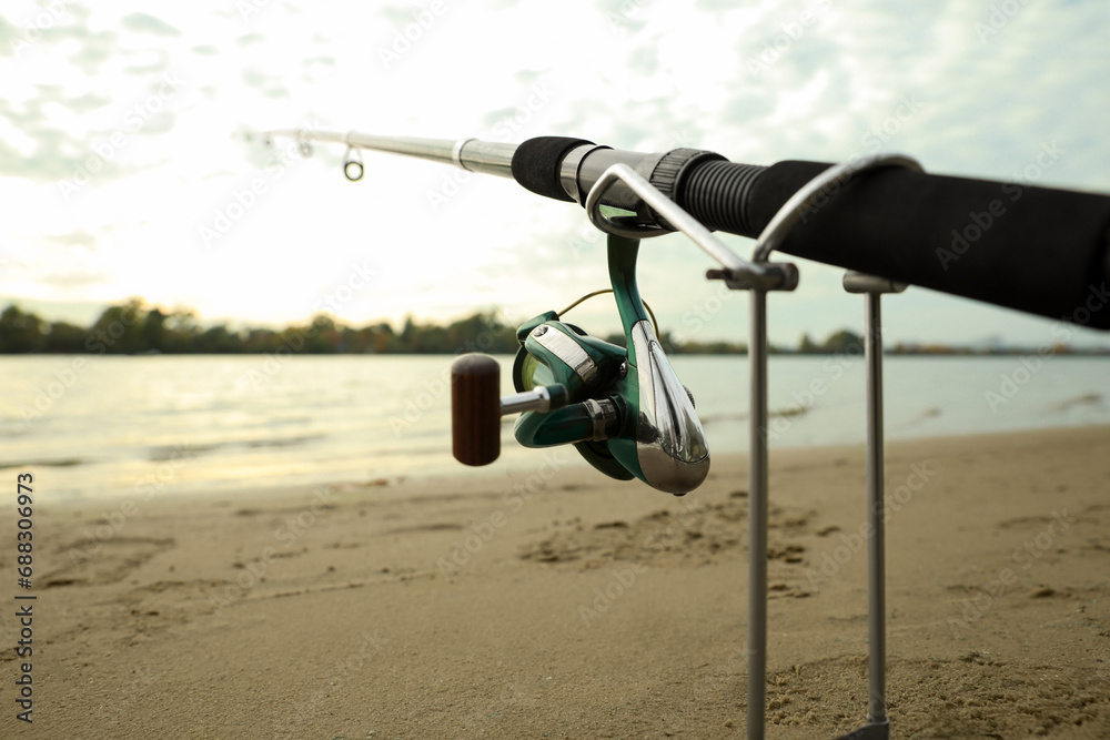 Fishing rod with reel on sand near river, closeup. Space for text
