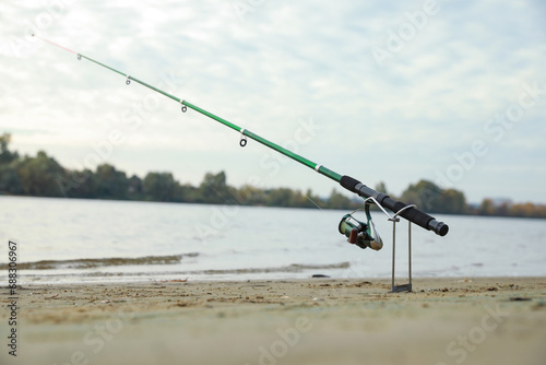 Fishing rod with reel on sand near river, space for text