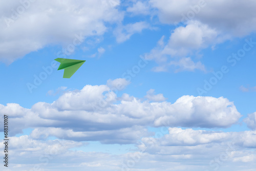 Green paper plane flying in blue sky with clouds