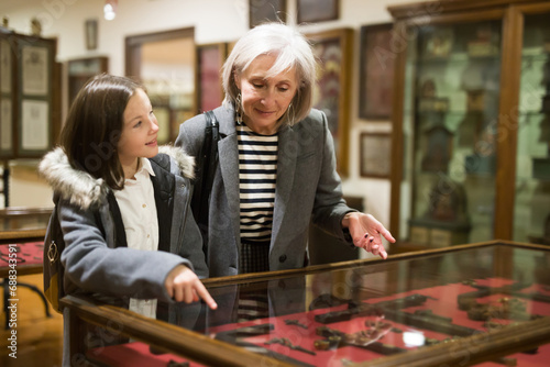 Friendly aged female tutor helping preteen girl exploring antique showpieces in local history museum.. photo