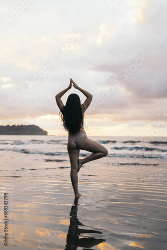 Rear view of a brunette woman doing yoga on the beach