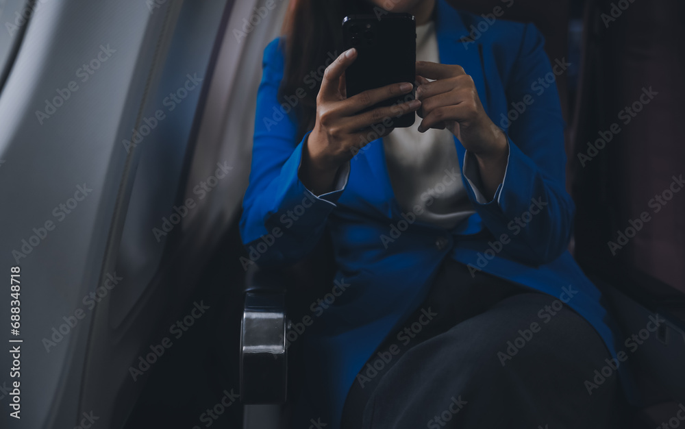 Obraz premium Young Asian business woman talking on smartphone, businesswoman working while flying at plane, Young woman using the internet at airplane, Air travel, long flight.