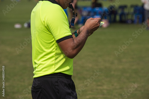 Professional soccer referee on a pitch of a youth soccer tournament. After team scores a goal  referee takes a note regarding to a match s score and a score player.