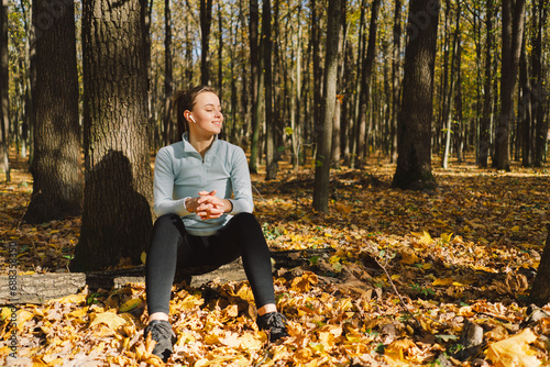 Beautiful girl listening to music and doing fitness outdoors in a sunny autumn forest. Body positive, sports for women, harmony, healthy lifestyle, self-love and wellness.