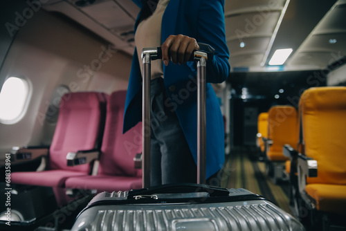 Asian female traveler putting luggage into overhead locker on airplane during boarding.