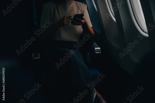 Attractive Asian female passenger of airplane sitting in comfortable seat while working laptop and tablet with mock up area using wireless connection. Travel in style, work with grace.