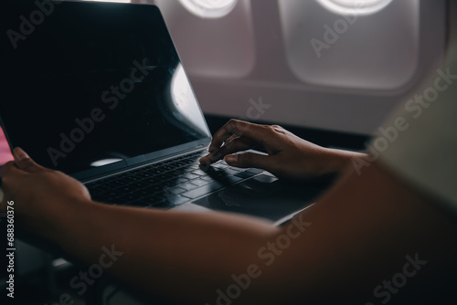 Asian woman passenger sitting in airplane near window and reading news from social networks or using travel applications in smartphone