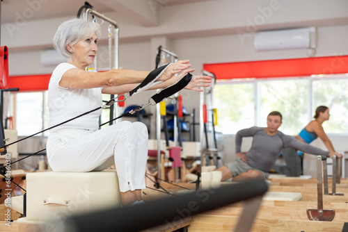 Elderly athletic woman working out with straps in pilates studio..