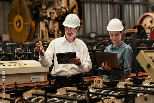 Factory engineer manager with assistant using laptop to conduct inspection of steel industrial machine  exemplifying leadership as machinery engineering inspection supervisor in metalwork manufacture.