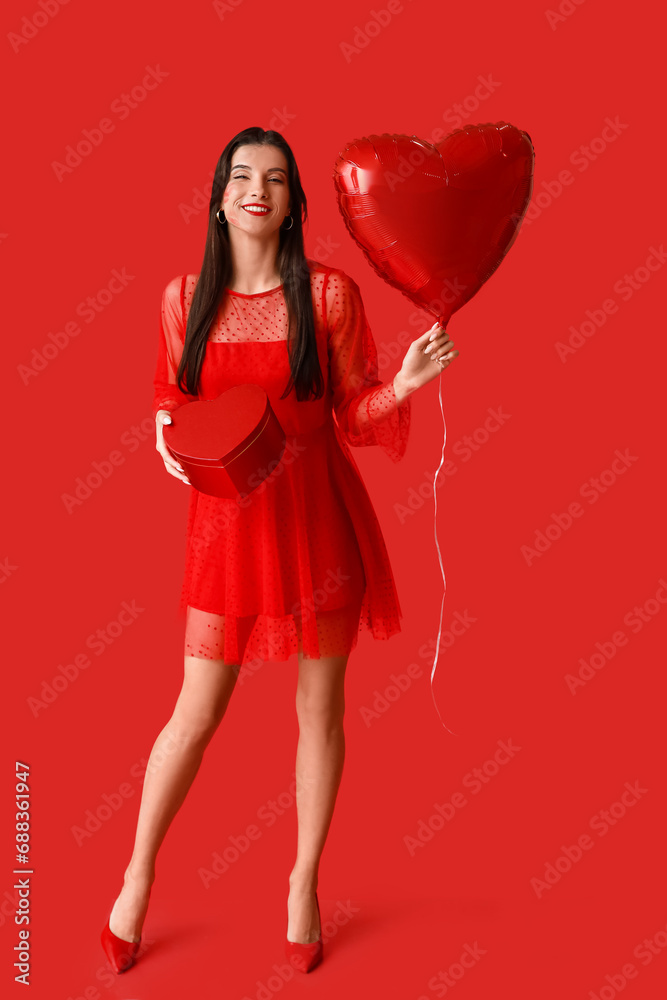Beautiful young woman with kiss marks on her face holding gift box and heart shaped air balloon on red background Beautiful young woman with kiss marks on her face holding gift box and heart shaped air balloon on red background