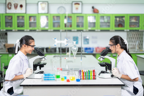 Vaccine and virus research in the lab of two Asian female scientists using a microscope to look at germs There are equipment such as glass tubes, beakers, and chemicals in medical biology.