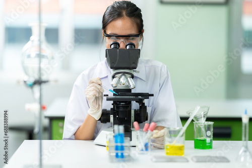 Asian female scientist is a student doing lab experiments with a microscope. Holding a glass tube and dripping a chemical solution for a biology lab There are glass tubes and beakers. Medical work