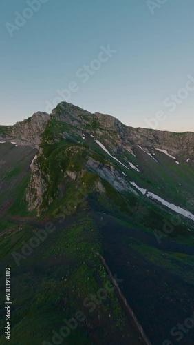 Vertical video. Aerial view mountain ridge peak ski resort cable car extreme close rock natural wall stone texture snow sunset. FPV sport drone amazing shot cliff alpine valley morning sunrise grass photo