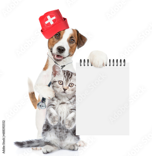 Funny jack russell terrier dressed like a doctor with stethoscope on his neck hugs tiny kitten and shows empty notebook. isolated on white background © Ermolaev Alexandr