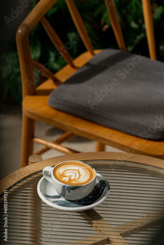 Cup of hot coffee latte on glass table and beautiful latte art with afternoon light in the cafe. © Korradol