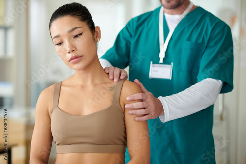 Rehab center worker palpating shoulder of sportswoman suffering with chronic pain after injury