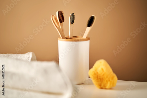 Bamboo toothbrushes in a cup and a towel in a bathroom interior.