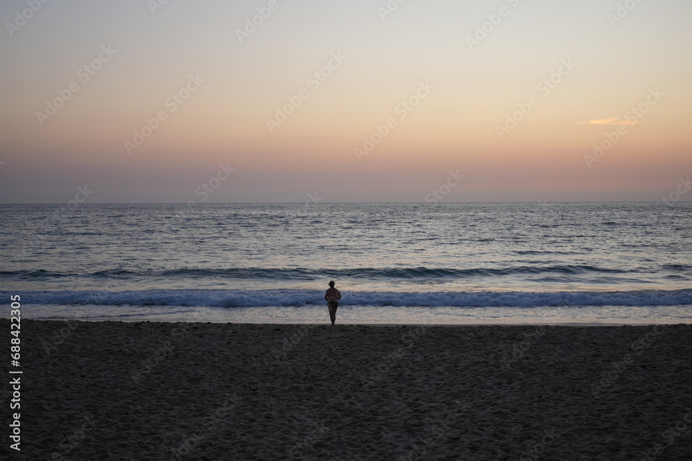 A person walking on the beach at sunrise, Bondi Beach, Sydney Australia 