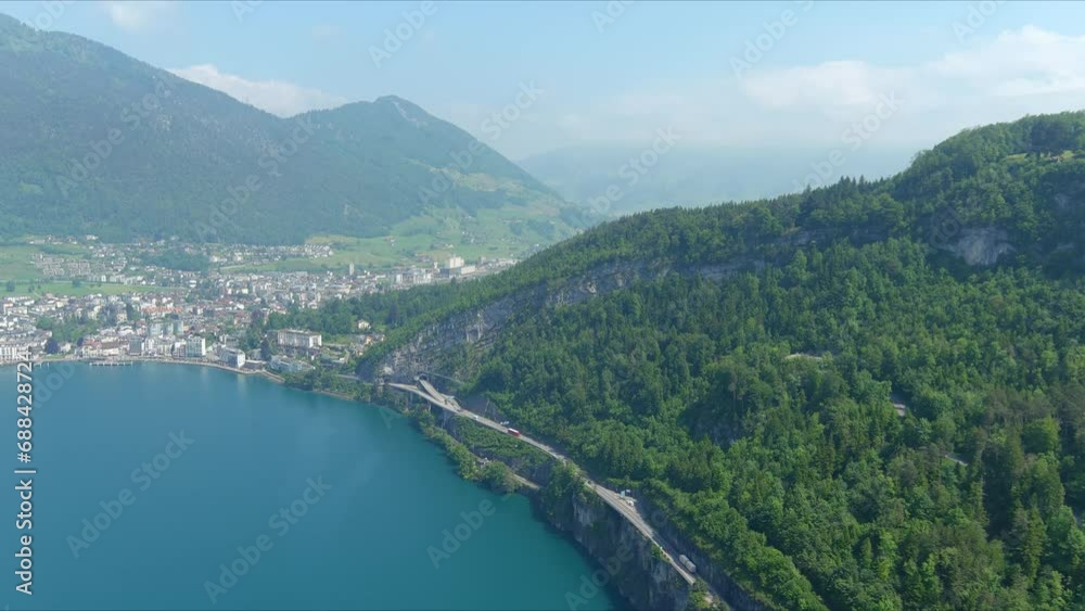 Morschach Flyover: Moving Over Scenic Water Valley Towards Alps Mountains, Switzerland, Europe, Drone | Closer Inland Movement Along Road Cliffside Beside Majestic Blue Lake Morschach Flyover: Moving Over Scenic Water Valley Towards Alps Mountains, Switzerland, Europe, Drone | Closer Inland Movement Along Road Cliffside Beside Majestic Blue Lake