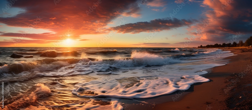 Stormy conditions along the Baltic sea shore reveal a stunning sunset sky with glowing clouds, golden sunlight, crashing waves, and a picturesque panoramic view of the seascape and cloudscape