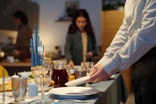 Close-up of young man putting plates on table served for Hanukkah dinner while helping his family with preparations photo