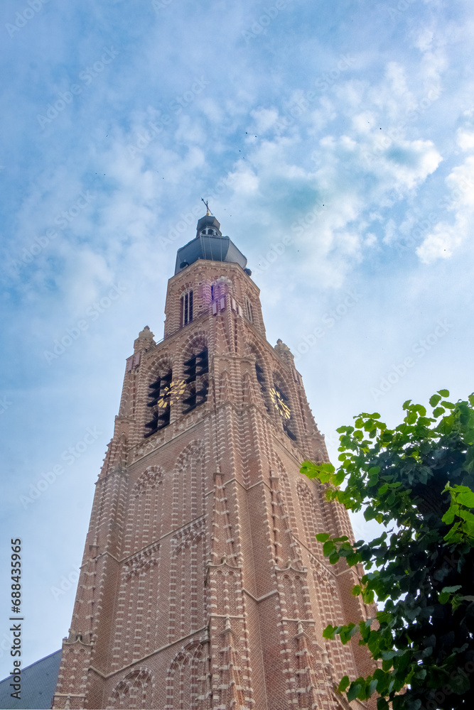 Captured in this image is the awe-inspiring tower of the church in Hoogstraten, a striking example of Gothic architecture. As the tower ascends towards the heavens, its intricate brickwork and