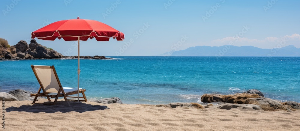Umbrella and chair on Agios Stefanos Beach with Kastri ruins and scenic coast in Kos, Greece.