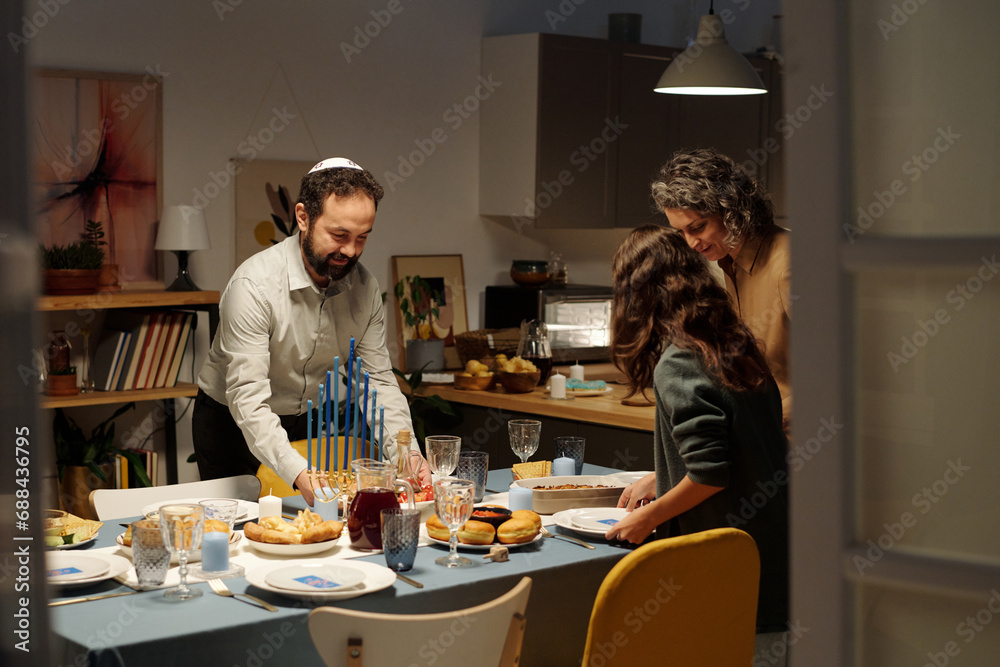 Jewish family of three serving table for Hanukkah dinner with homemade food in living room while preparing for receiving guests