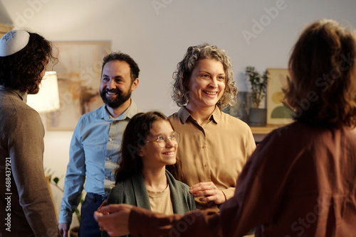 Happy mature woman and her little daughter looking at young female guest with smiles while meeting and greeting her in living room photo