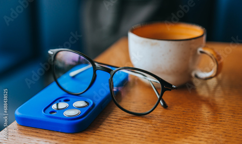 Close up picture of glasses, phone and coffee cup placed on table at cafe.