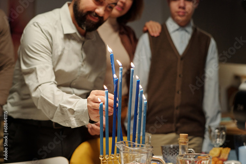 Cropped shot of mature man putting ninth candle on menorah candlestick standing on table served with homemade food for Hanukkah photo