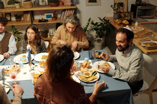 High angle of Jewish family gathered by served table having homemade food and discussing something during Hanukkah celebration photo