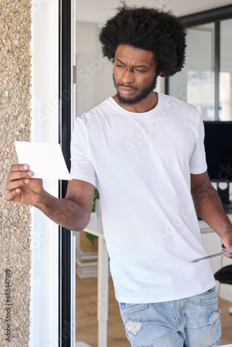 portrait of a black entrepreneur with afro and casual look holding and looking at a photo while leaning on the wall in a relaxed manner photo